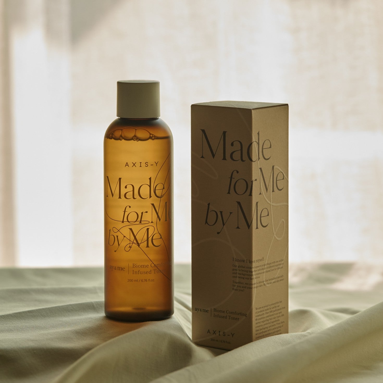 Bottle and box of 'Made for Me by Me' product on a soft fabric background