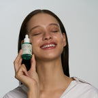 Woman holding a skincare dropper bottle against a plain background